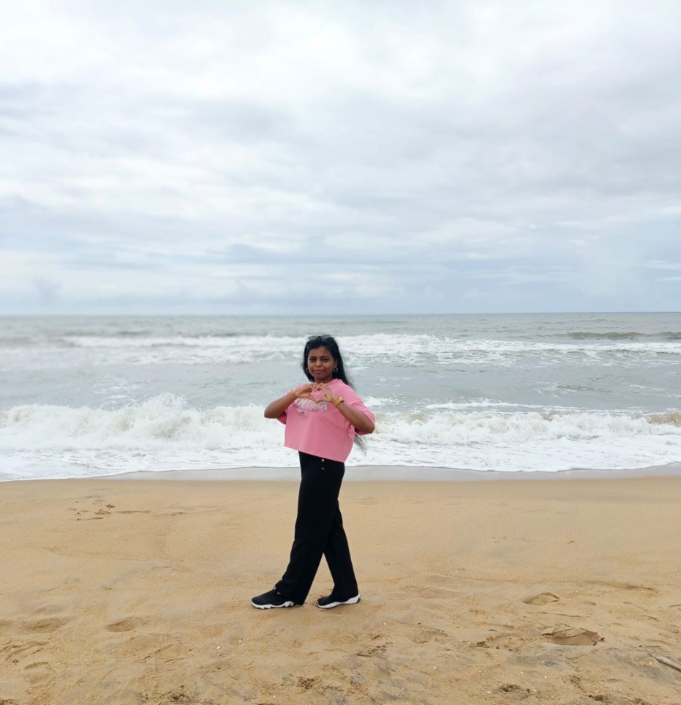 Sivamathi making a heart with her hands at the beach